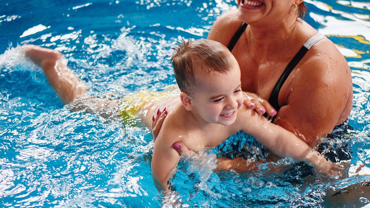 a young boy swimming in a pool with a parent