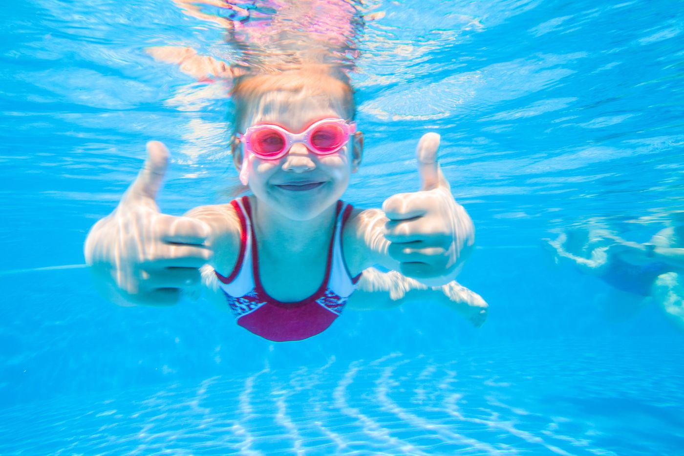 a young kid swimming while giving two thumbs up