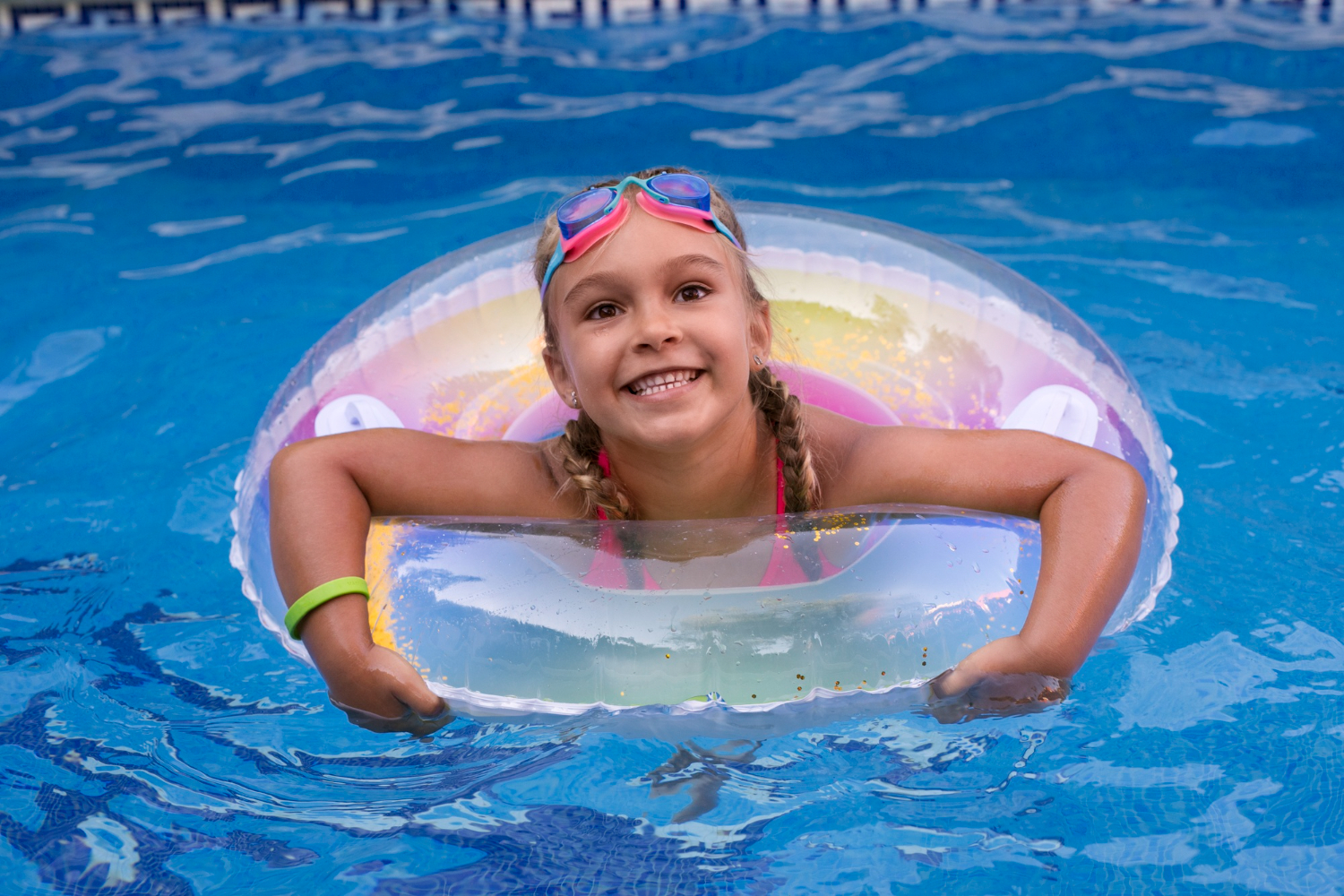 young girl swimming with pool floaty looking up and smiling